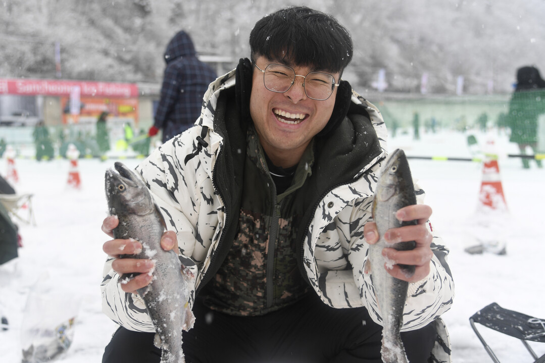  눈을 맞으며 산천어 얼음낚시에 빠져있는 관광객