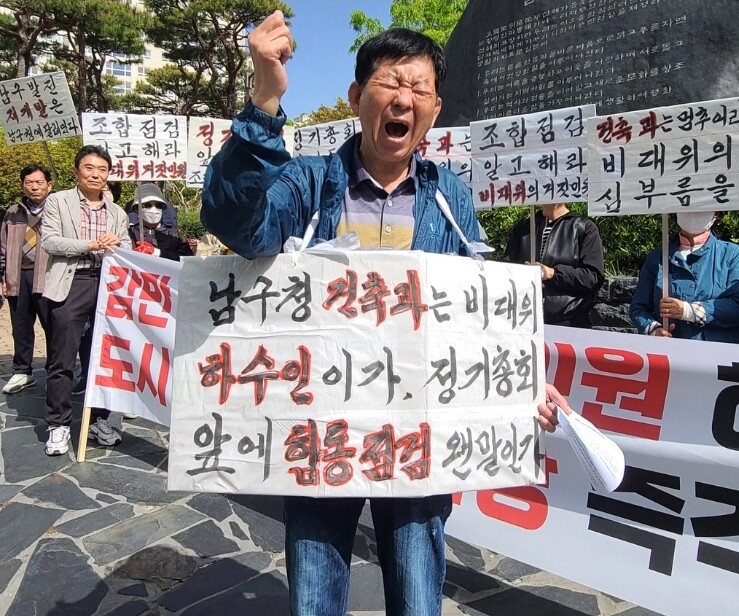 부산 남구 감만1구역재개발조합 뉴스테이(기업형 임대주택)를 추진하는 현 집행부 소속 조합원 60여명이 21일 오전 남구청사 정문 인근에서 ‘감만비대위의 악성민원 해결사 자처한 도시국장·건축과장 즉각 사퇴하라’라고 적힌 현수막을 앞세운 채 정기총회를 앞둔 시점에 난데없는 ‘합동점검’을 진행하는 데 대한 항의집회를 열고 있다. 60대로 보이는 한 초로의 뉴스테이 재개발사업 지지 조합원이 앞으로 나서 ‘남구청 건축과는 비대위의 하수인인가. 정기총회 앞에 합동점검 웬말인가’라고 적은 대형 수제 종이포스터를 목에 건 채 한이 맺힌 듯 “위법단체 비대위 편드는 도시국장, 건축과장은 즉각 사퇴하라”라고 절규하듯 외치고 있다.