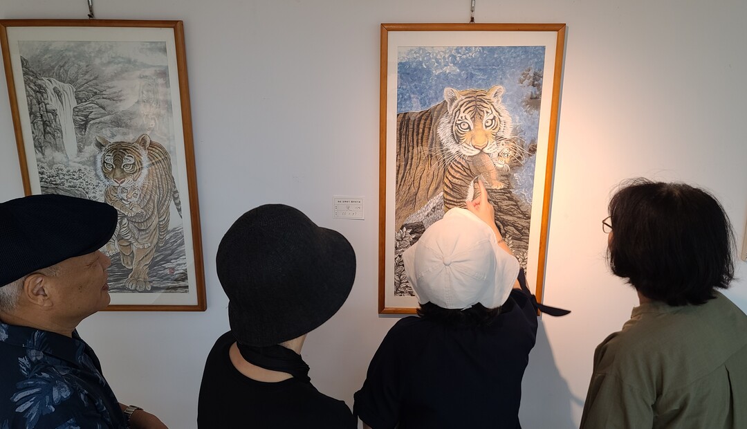 지난 15일 부산시민공원 내 예술촌 갤러리2에서 ‘제7회 덕곡 김흥식 개인전’의 문을 연 뒤 전시장을 찾은 시민들이 어린 새끼를 입에 물고 안전한 곳으로 이동하는 어미 호랑이의 ‘새끼 사랑 동물심’을 담은 호화 앞에서 김흥식(사진 왼쪽) 화백의 설명을 듣고 있다.