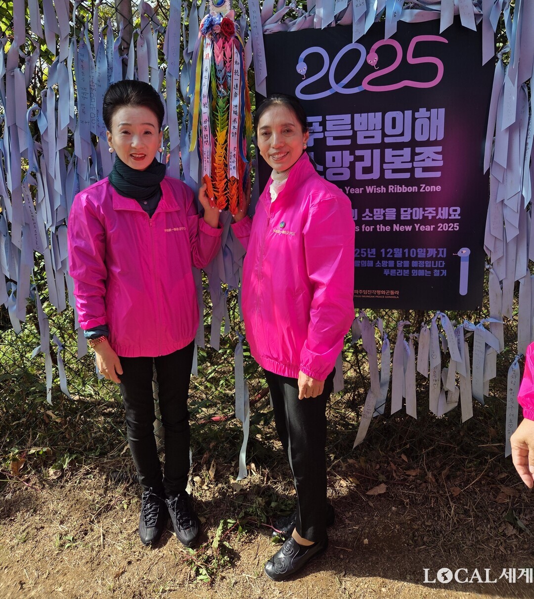 강경희 회장과 박은자 국장이 비무장지대를 따라 뻗어 있는 철책선 철조망에 평화통일에 대한 염원을 담은 1천 마리의 종이학을 걸어 놓고 기념사진을 촬영하고 있다.